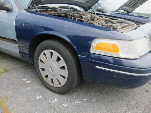 2001 Ford Crown Victoria - A blue Ford Crown Victoria with its hood open, revealing the engine compartment, sits next to another vehicle.