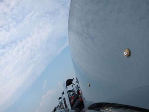 2001 Ford Crown Victoria - Multiple white trucks are lined up, with the camera focused on the large, reflective surface of one vehicle against a backdrop of clouds.