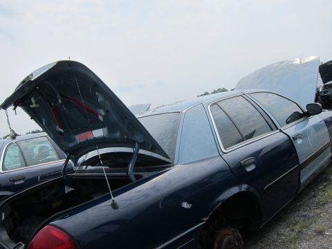 2001 Ford Crown Victoria - A dark blue Ford Crown Victoria sits in a junkyard with its trunk and hood open, showing signs of wear and tear.