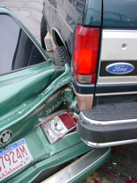 1995 Ford Bronco - The rear of a green car is crushed after a collision with a Ford truck.