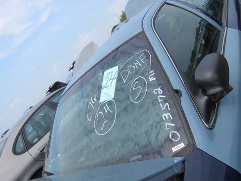 2001 Ford Crown Victoria - Handwritten markings and a sticker are visible on the windshield of a car in a junkyard.