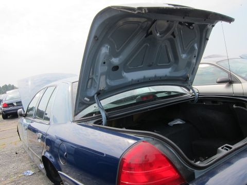 2001 Ford Crown Victoria - The trunk and hood of a blue sedan are open, revealing the interior of the trunk and the engine bay. Another vehicle is parked behind it.