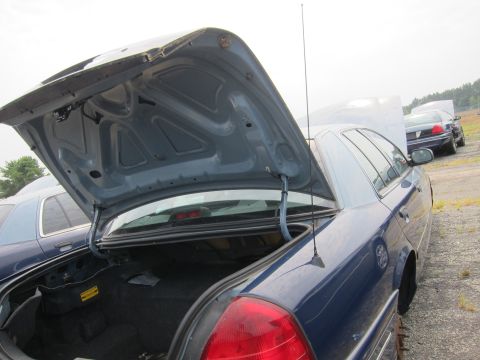 2001 Ford Crown Victoria - A blue 2001 Ford Crown Victoria is parked with its trunk and hood open, alongside other vehicles.