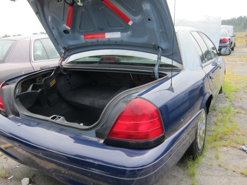 2001 Ford Crown Victoria - Rear view of a blue 2001 Ford Crown Victoria with its trunk open, showing the interior of the trunk.