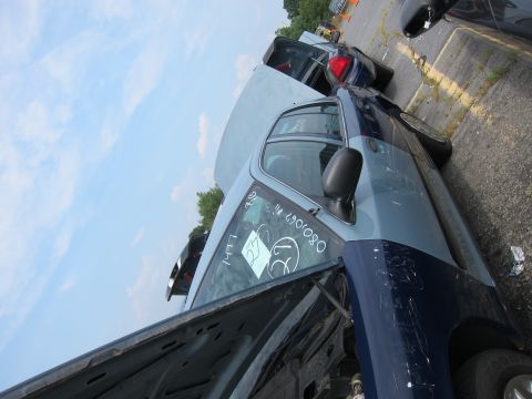 2001 Ford Crown Victoria - A two-tone blue 2001 Ford Crown Victoria sits in a junkyard with its hood open, alongside other vehicles.