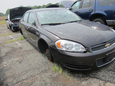 2001 Ford Crown Victoria - Junkyard scene with a dark sedan missing wheels and another vehicle in the background.
