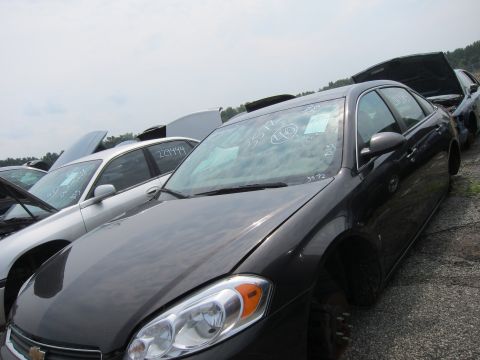 2001 Ford Crown Victoria - Several cars are parked in a junkyard, with their hoods open under an overcast sky.
