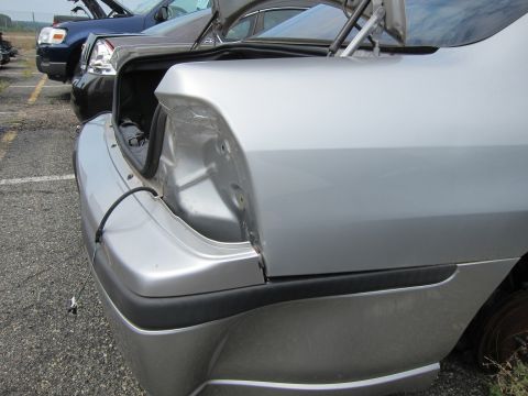 2001 Ford Crown Victoria - A silver sedan's rear quarter panel is visible with the trunk open, revealing damage and a missing taillight assembly.