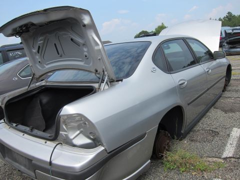 2001 Ford Crown Victoria - Junkyard sedan with open trunk and hood, missing wheels, under a cloudy sky.