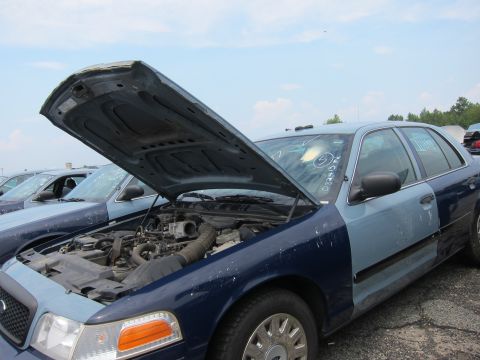 2001 Ford Crown Victoria - Junkyard scene with two Ford Crown Victorias, one with its hood open, revealing the engine compartment.