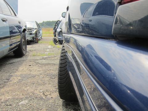 2001 Ford Crown Victoria - Close-up of a 2001 Ford Crown Victoria's rear tire and body panel in a junkyard setting.