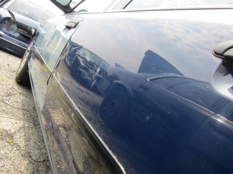 2001 Ford Crown Victoria - A dark blue 2001 Ford Crown Victoria shows significant damage to its side door, with visible scratches and a dent.