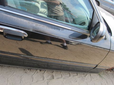 2001 Ford Crown Victoria - The side of a black sedan shows peeling paint and a chrome door handle. A person's reflection is visible in the window.