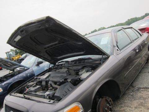 2001 Ford Crown Victoria - Two Ford Crown Victorias sit in a junkyard, hoods open, revealing their engines.