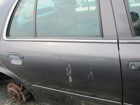2001 Ford Crown Victoria - Side view of a gray 2001 Ford Crown Victoria showing damage to the door and a missing front wheel.