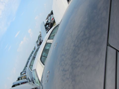 2001 Ford Crown Victoria - Multiple vehicles are lined up in a junkyard, with a focus on the side of a dark-colored car in the foreground.