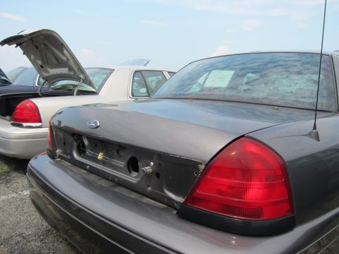 2001 Ford Crown Victoria - Two Ford Crown Victorias are parked side-by-side, one with its trunk open, under a cloudy sky.