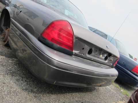 2001 Ford Crown Victoria - Grey 2001 Ford Crown Victoria in a junkyard, missing bumper and rear wheel. Another car is visible behind it.