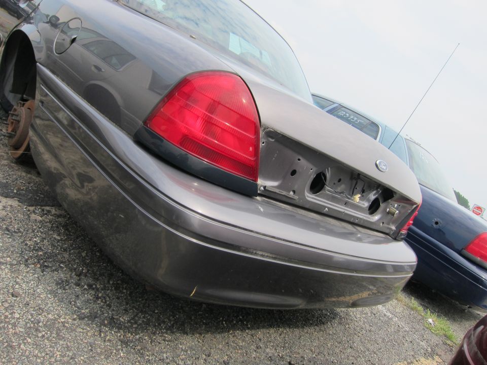 Rear view of a grey 2001 Ford Crown Victoria with no license plate or bumper, and a blue car behind it