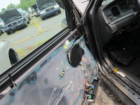 2001 Ford Crown Victoria - The interior door panel of a car is removed, exposing wires and a speaker, with other vehicles in the background.