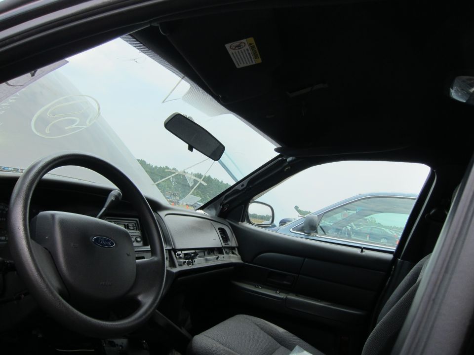 Interior of a 2001 Ford Crown Victoria, showing the steering wheel, dashboard, and passenger door. A second vehicle is visible through the window