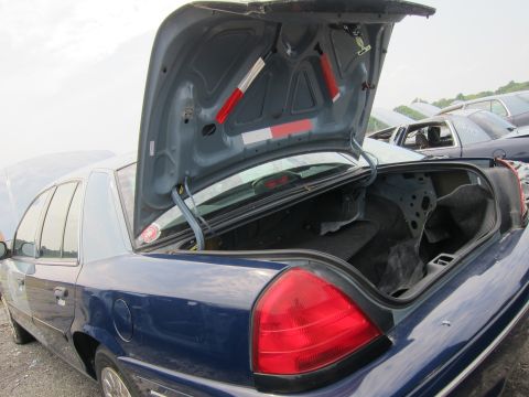 2001 Ford Crown Victoria - The rear of a blue 2001 Ford Crown Victoria is visible with its trunk open, revealing a damaged interior.