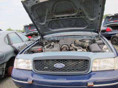 2001 Ford Crown Victoria - The front of a 2001 Ford Crown Victoria is shown with its hood open, revealing the engine and a prominent Ford grille.