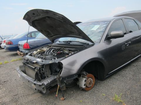 2001 Ford Crown Victoria - Junkyard car with missing front bumper and wheel, hood open, showing engine compartment.