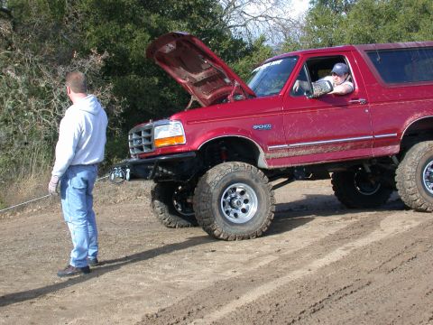 1996 Ford Bronco - A red 1996 Ford Bronco is shown with its hood raised, a lifted suspension and large off-road tires on a dirt track.