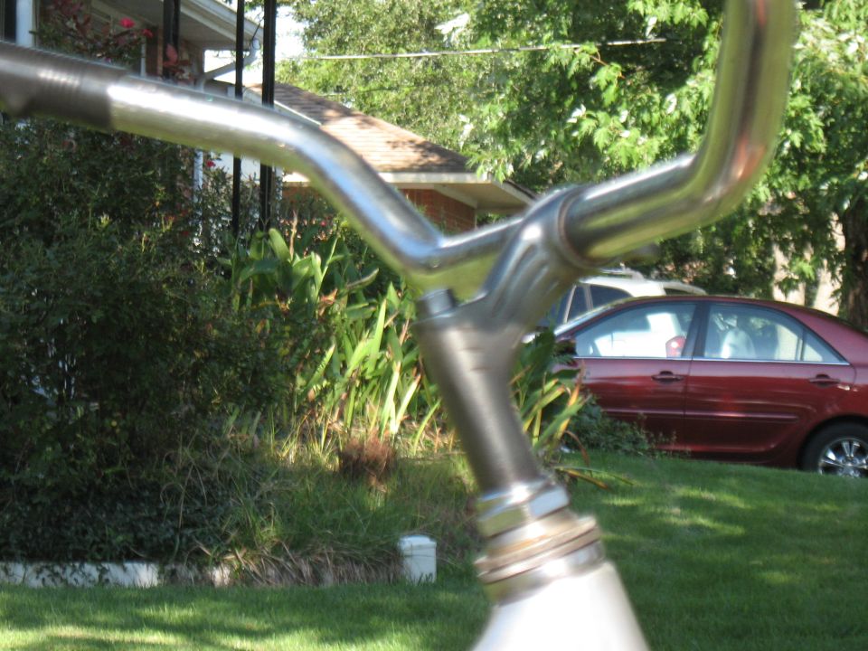 Close-up of chrome bicycle handlebars with a red car in the background