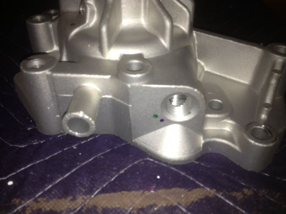 Close-up of a silver metal automotive part with several ports and bolt holes. It sits on a dark, quilted fabric