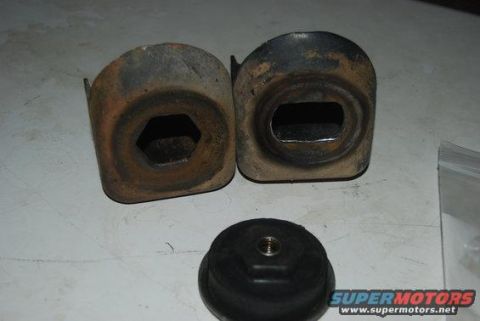 1982 Ford Bronco - Two metal brackets with hexagonal and rectangular openings, alongside a rubber mount, are displayed on a surface.