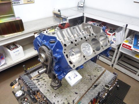 1982 Ford Bronco - A close-up view of a blue engine block assembly, pistons, a timing chain, and an oil filter, resting on a workbench with tools.