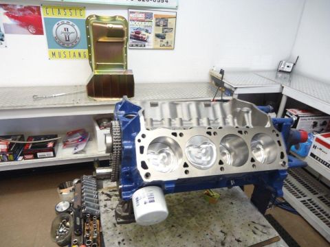 1982 Ford Bronco - A blue engine block with pistons and an oil filter sits on a workbench, surrounded by tools and engine parts.