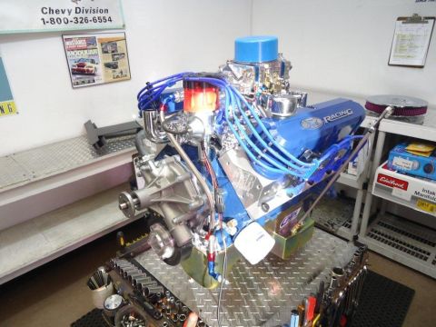 1982 Ford Bronco - A blue Ford Racing V8 engine is displayed on a metal stand, surrounded by tools and engine parts.
