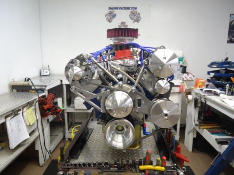 1982 Ford Bronco - A custom V8 engine is displayed on a stand in a workshop, surrounded by tools and equipment.