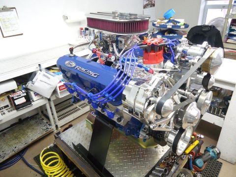 1982 Ford Bronco - A custom V8 engine with 'Ford Racing' valve covers is displayed on a stand in a workshop.