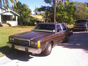 1987 Ford Crown Victoria LTD - A brown sedan is parked outside a house on a clear day with another vehicle in the background.
