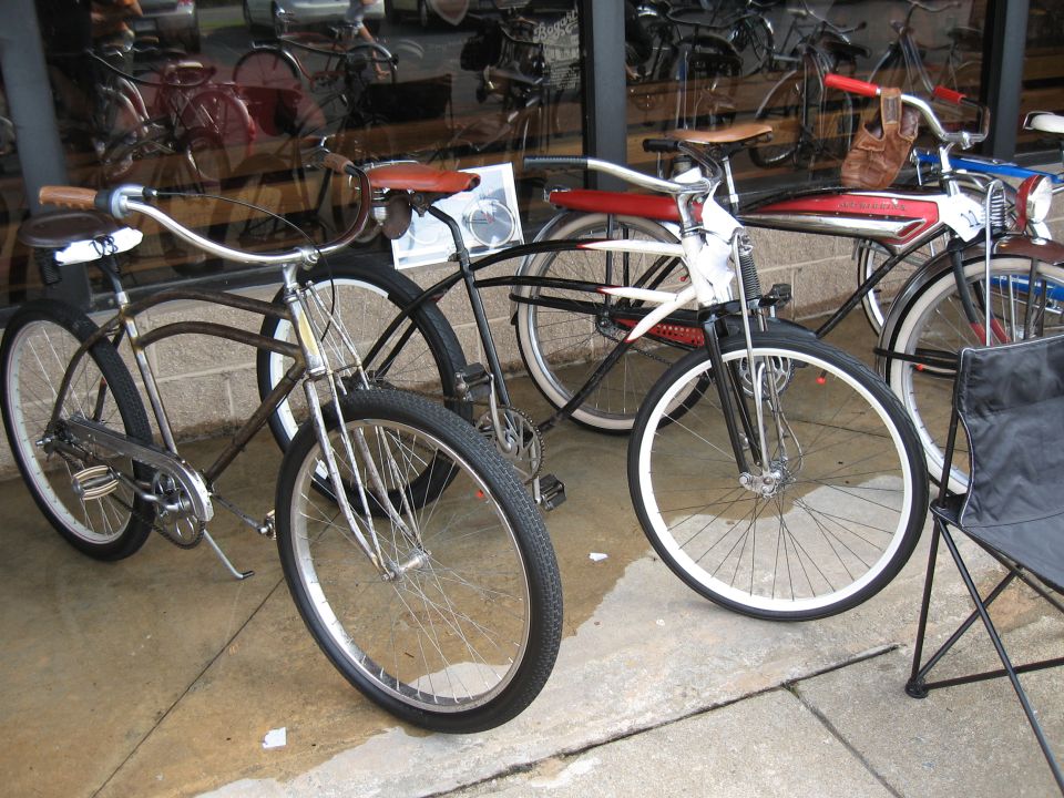 Several vintage bicycles parked outside a shop, some with chrome fenders and leather seats