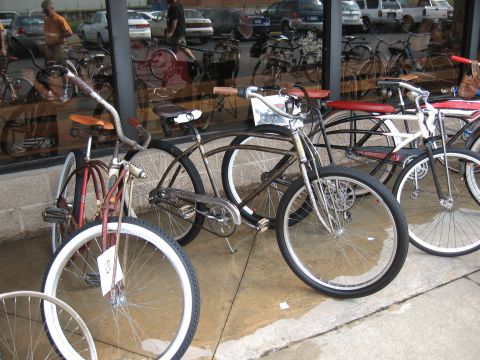 Several vintage bicycles displayed outside a building with reflections of cars in the window