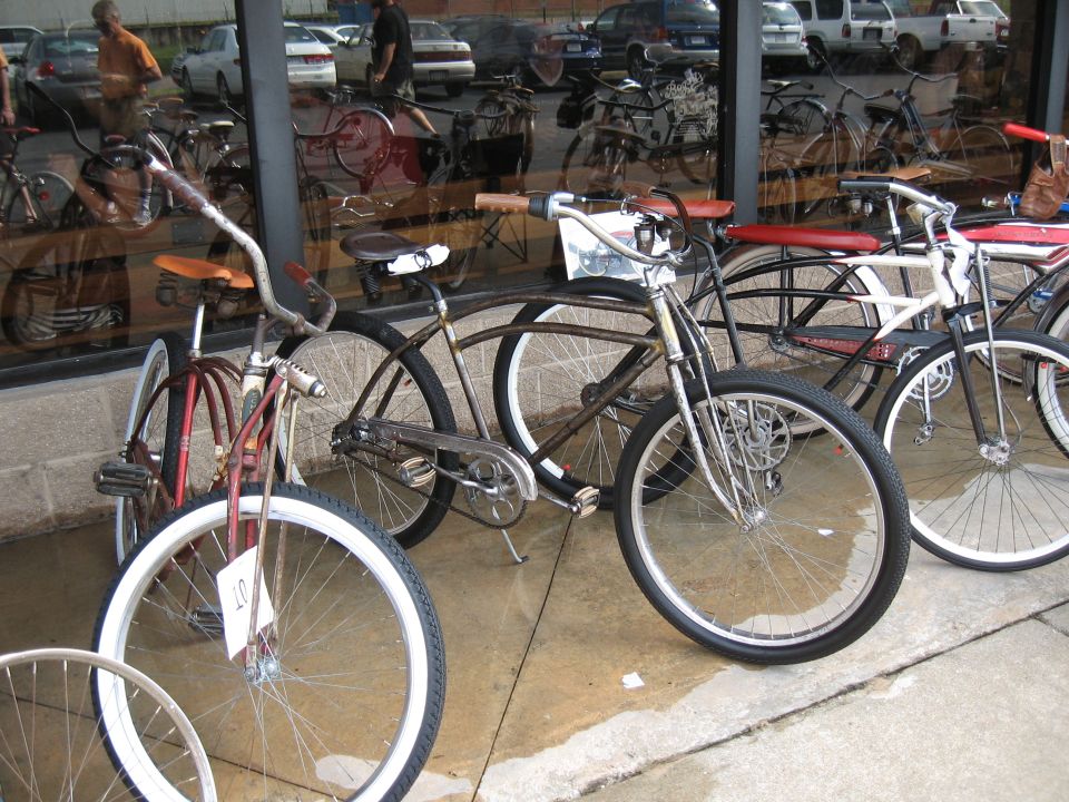 Several vintage bicycles displayed outside a building with reflections of cars in the window