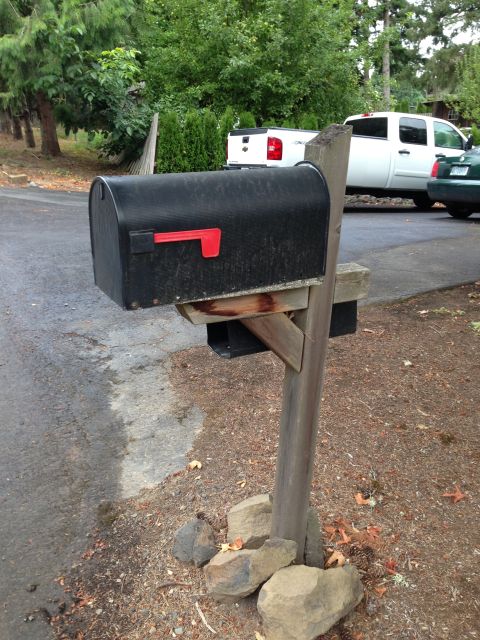 1992 Ford F-150 - Black mailbox with red flag up on a weathered leaning wooden post by a road, a white pickup parked in the background.