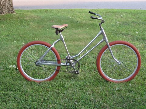 Silver bicycle with red tires and brown seat parked on grass