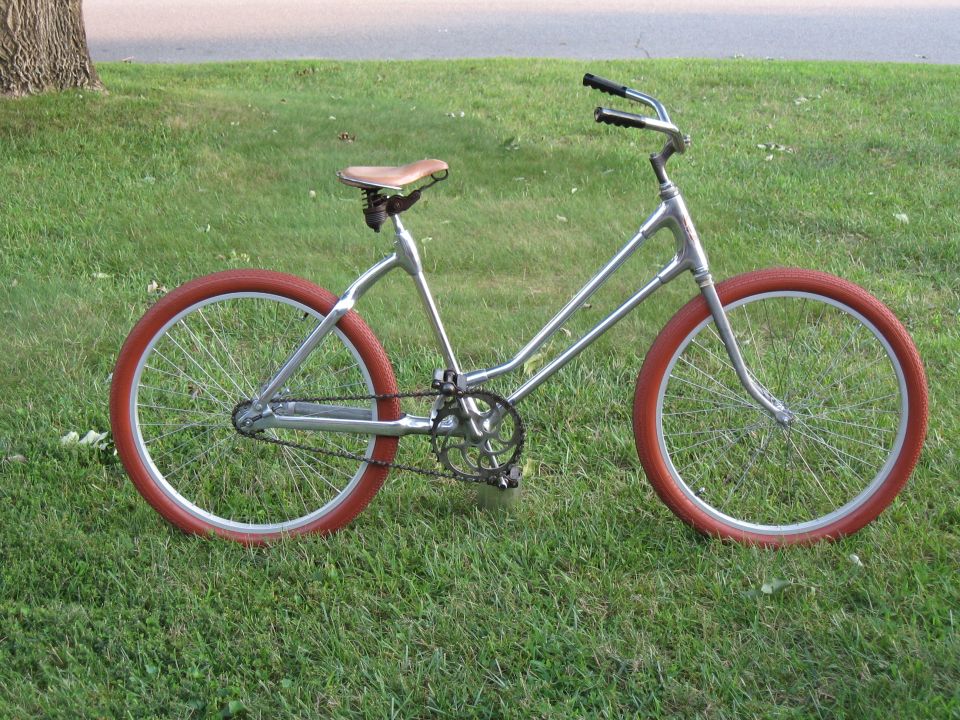 Silver bicycle with red tires and brown seat parked on grass