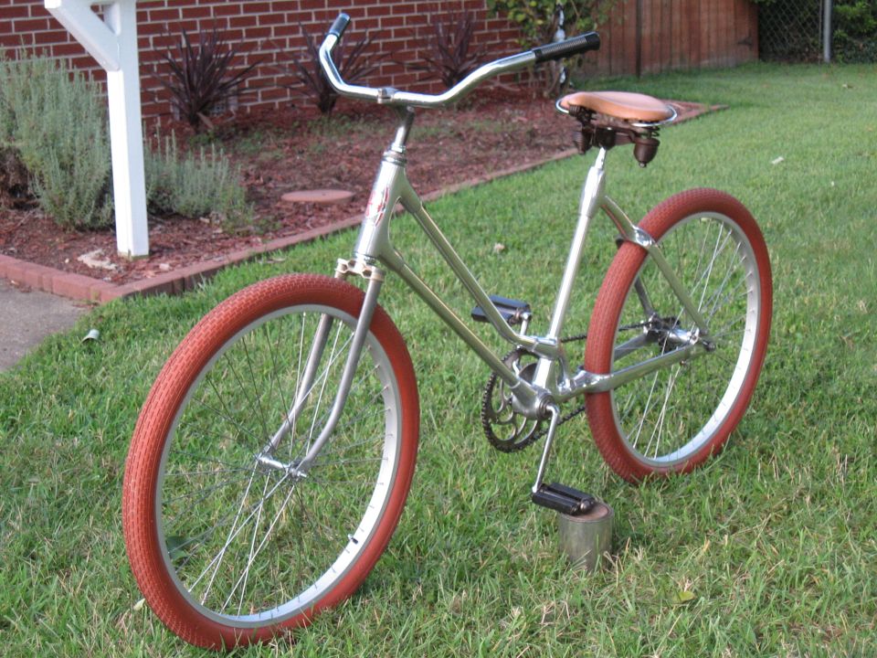 Silver bicycle with red tires and a brown seat, parked on grass
