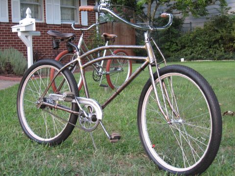 Two cruiser bicycles with chrome handlebars and brown seats parked on grass