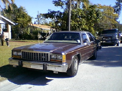 1987 Ford Crown Victoria LTD - A brown 1983 Ford Crown Victoria sedan is parked on a street with a house and trees in the background.