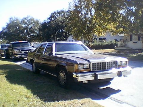 1987 Ford Crown Victoria LTD - A 1987 Ford Crown Victoria LTD is parked on the street, with a truck visible in the background.
