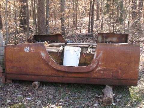 1957 Ford F-100 - A heavily rusted truck bed sits outdoors, supported by logs amidst trees and fallen leaves.