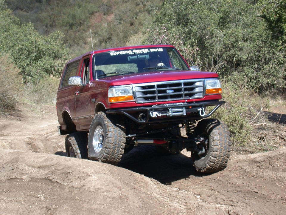 Red Ford Bronco flexing on a dirt trail with tube winch bumper and mud-terrain tires